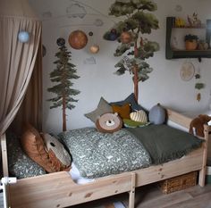 a child's bedroom with a tree mural on the wall and stuffed animals on the bed