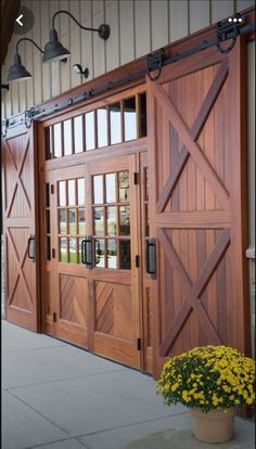 a large wooden garage door next to a potted plant with yellow flowers in it