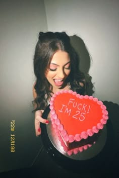 a woman holding a heart shaped cake with the words f k i m 25 on it