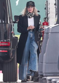 a woman in black jacket and jeans standing next to a van with her hand on her hip