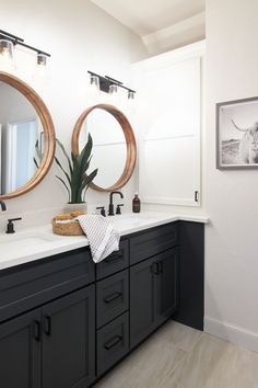 a bathroom with two round mirrors above the sinks and black cabinetry on the wall