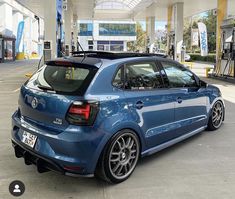 the back end of a blue car parked at a gas station with its hood up