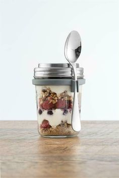 a glass jar filled with granola and yogurt next to a metal spoon