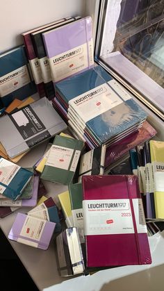 many books are stacked on top of each other in front of a window sill