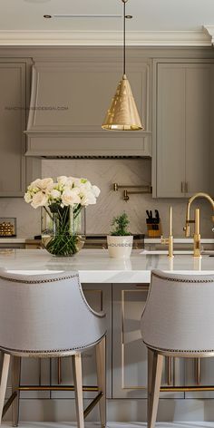 two white chairs sitting in front of a kitchen island with flowers on top of it