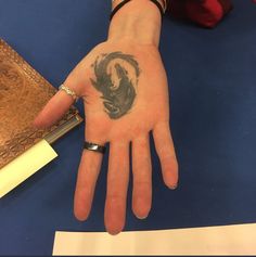 a person's hand with a tattoo on it sitting next to some papers and a pen