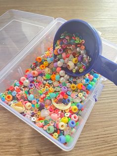 a plastic container filled with lots of different colored beads and button holes next to a blue measuring cup