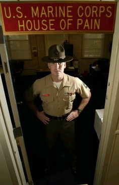 a man in uniform standing next to a sign that reads, pain lives here u s marine corp's house of pain