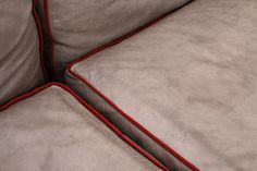 the corner of a gray couch with red piping on it's edges and two cushions