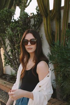 a woman wearing sunglasses standing next to a cactus