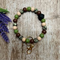 a bracelet with beads, charms and a key on a wooden table next to lavender flowers