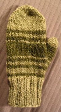 a green mitten sitting on top of a bed next to a pillow and blanket