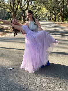 two women are dancing in the middle of the road with their arms around each other