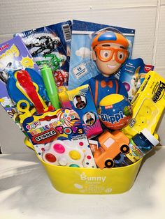 a yellow bucket filled with lots of toys and crafts on top of a white table