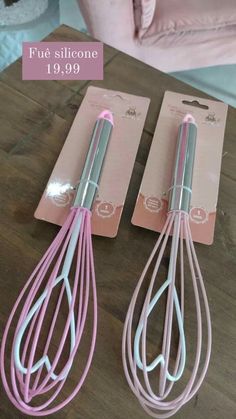 two pink and silver whisks sitting on top of a wooden table next to each other