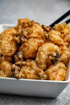 a white bowl filled with fried food and chopsticks on top of a table