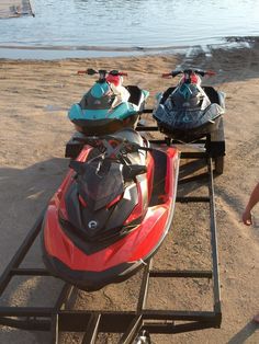 two snowmobiles parked next to each other on the sand at the water's edge