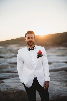 a man in a white tuxedo with a red rose on his lapel