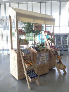 an outdoor fruit stand with fruits and vegetables on display in front of large windows at the airport