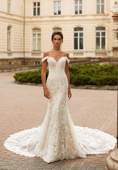 a woman in a white wedding dress standing on a brick walkway with her arms behind her back