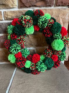 a green and red pom - pom wreath on a brick wall