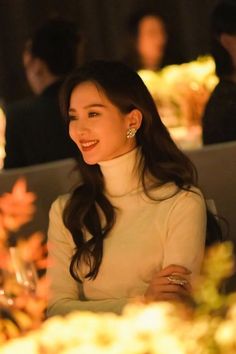 a woman sitting at a table with flowers in front of her and smiling for the camera