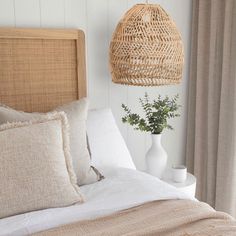 a wicker basket hanging over a bed next to a vase with a plant in it