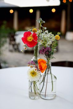 two vases filled with flowers sitting on top of a white table covered in lights