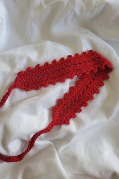 a red crocheted scarf laying on top of a white bed sheet covered in sheets