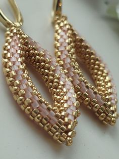 two pairs of pink and gold beaded earrings on a white surface with flowers in the background