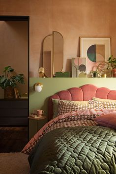 a bedroom with pink and green bedding, plants and pictures on the wall above it