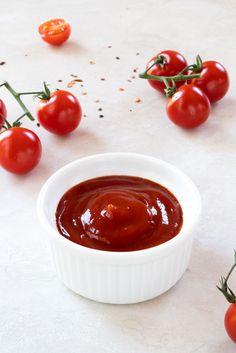 tomatoes and sauce in a small white bowl on a table with other tomatoes scattered around