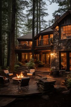 an outdoor fire pit in front of a large house with trees and rocks on the ground