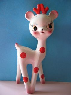 a white and red toy deer with a red bow on it's head sitting in front of a blue wall