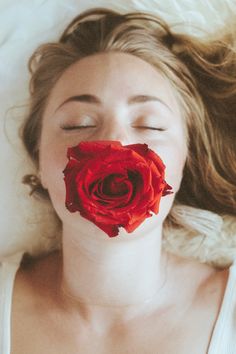 a woman laying in bed with her eyes closed and a red rose sticking out of her mouth