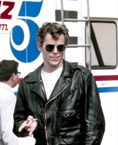 a man in black jacket and sunglasses standing next to a bus