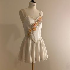 a white dress with flowers on the front and back, sitting on a mannequin