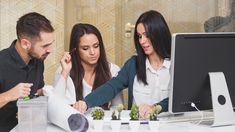 two women and a man are looking at something on the computer screen as they look at it