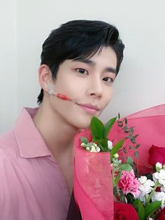 a young man holding a bouquet of flowers in front of his face and looking at the camera