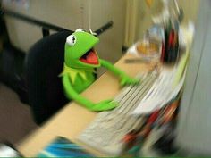 kermie the frog sitting at a desk with his arms outstretched and legs crossed