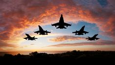 four fighter jets are flying in formation against a colorful sky with clouds at sunset or dawn