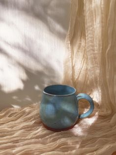 a blue mug sitting on top of a table next to a curtain and a window