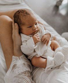 a woman holding a baby in her arms on top of a white sheeted bed