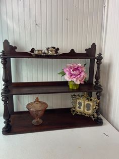 an old wooden shelf with flowers and other items on top of it in front of a white wall