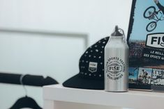 a silver bottle sitting on top of a white shelf next to a hat and other items