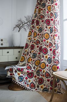 a white vase sitting on top of a table next to a window covered in a colorful blanket