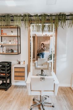 a woman is getting her hair done in a salon with greenery hanging from the ceiling