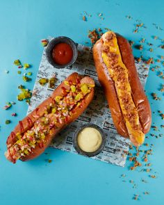 two hotdogs with condiments and ketchup on a blue surface