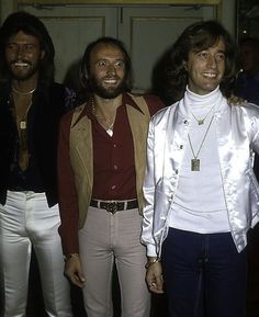 three men standing next to each other in front of a door wearing white pants and jackets