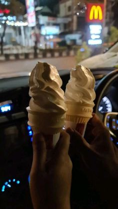 two ice cream cones are being held up in the car